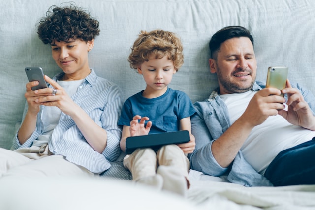 Parents sitting next to a child, playing on their phones