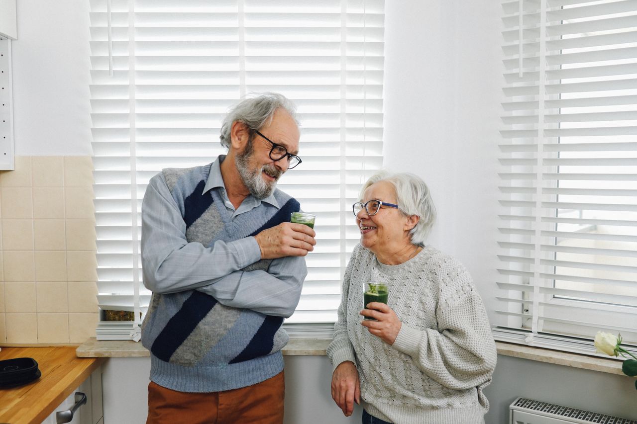 Senior couple smiling and enjoying green smoothies in a cozy kitchen setting
